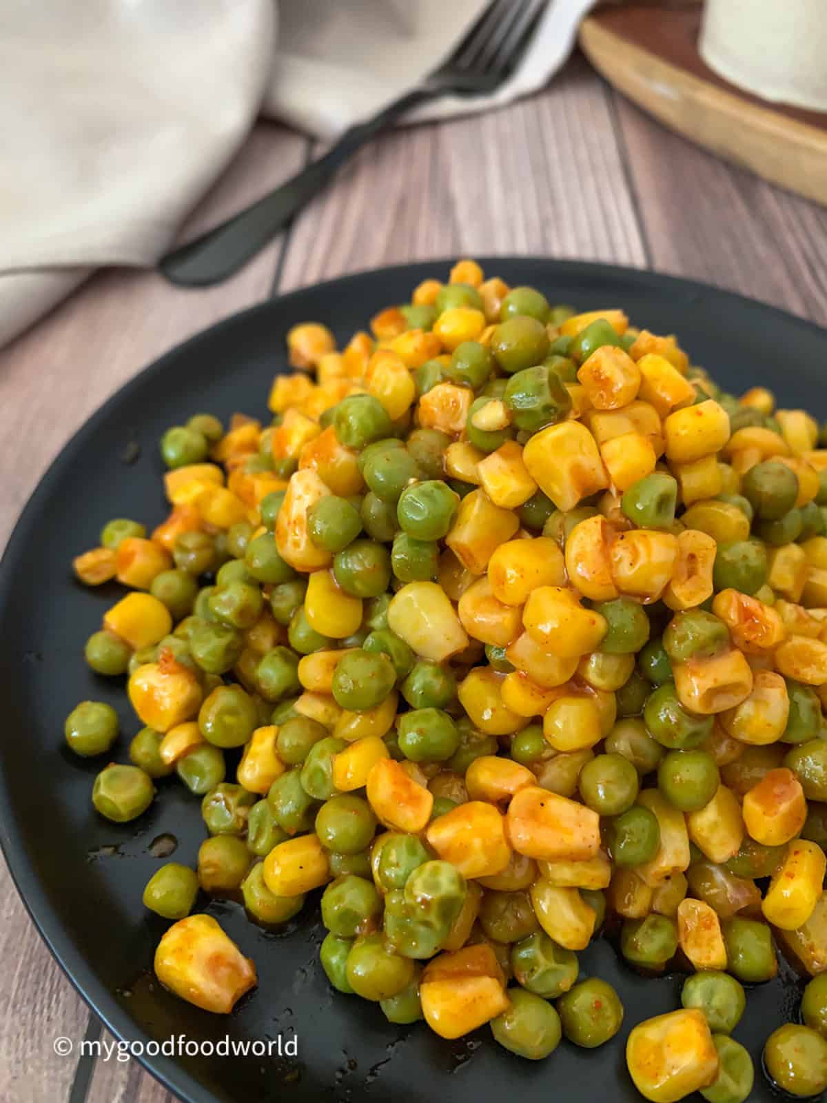 Juicy corn and peas salad is placed in a heap on a black plate.