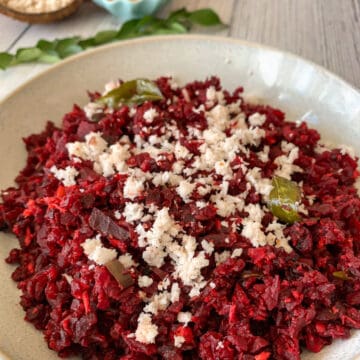 Beetroot sauteed in spices and topped with freshly grated coconut is placed in a round white bowl.