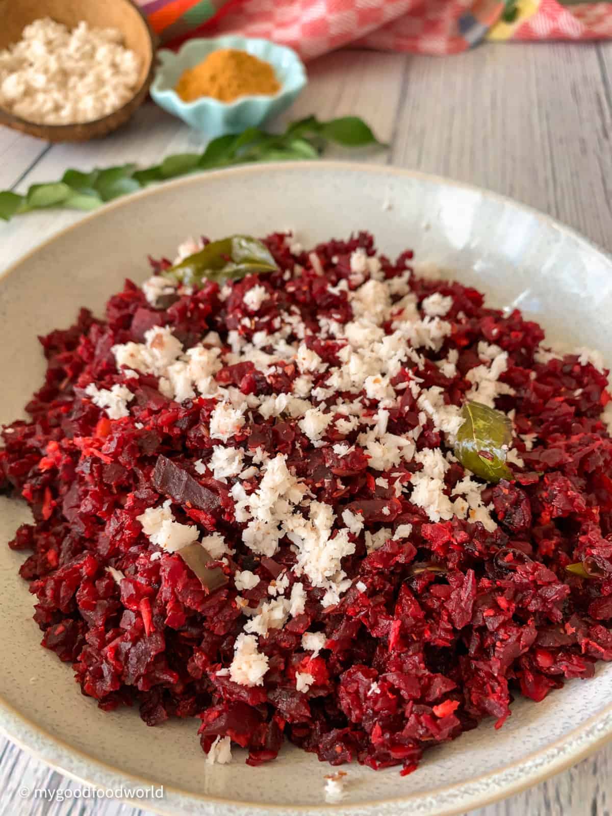 Beetroot sauteed in spices and topped with freshly grated coconut is placed in a round white bowl.