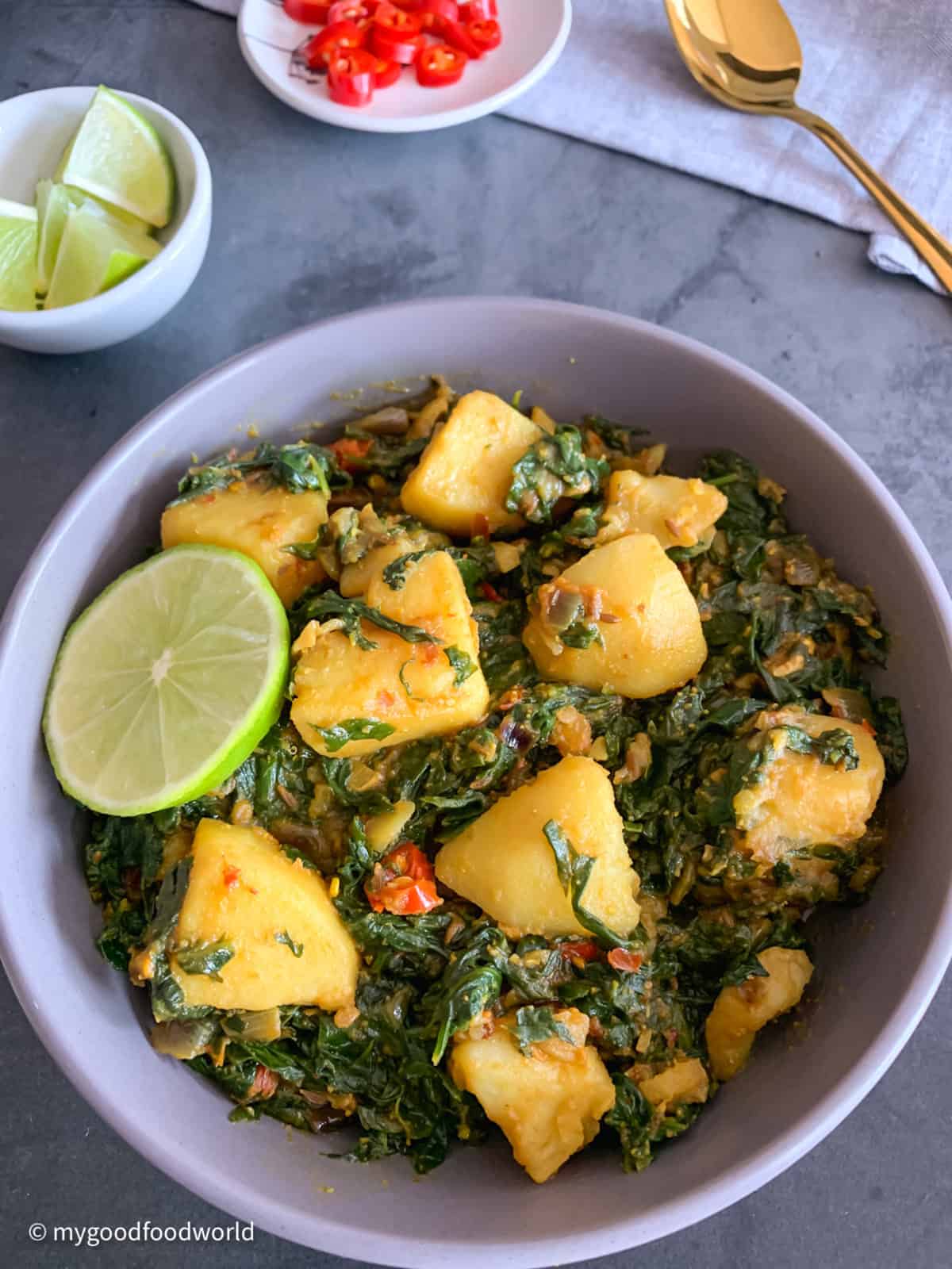 Cooked aloo palak sabzi placed in a round grey bowl with a cut piece of lemon as garnish.