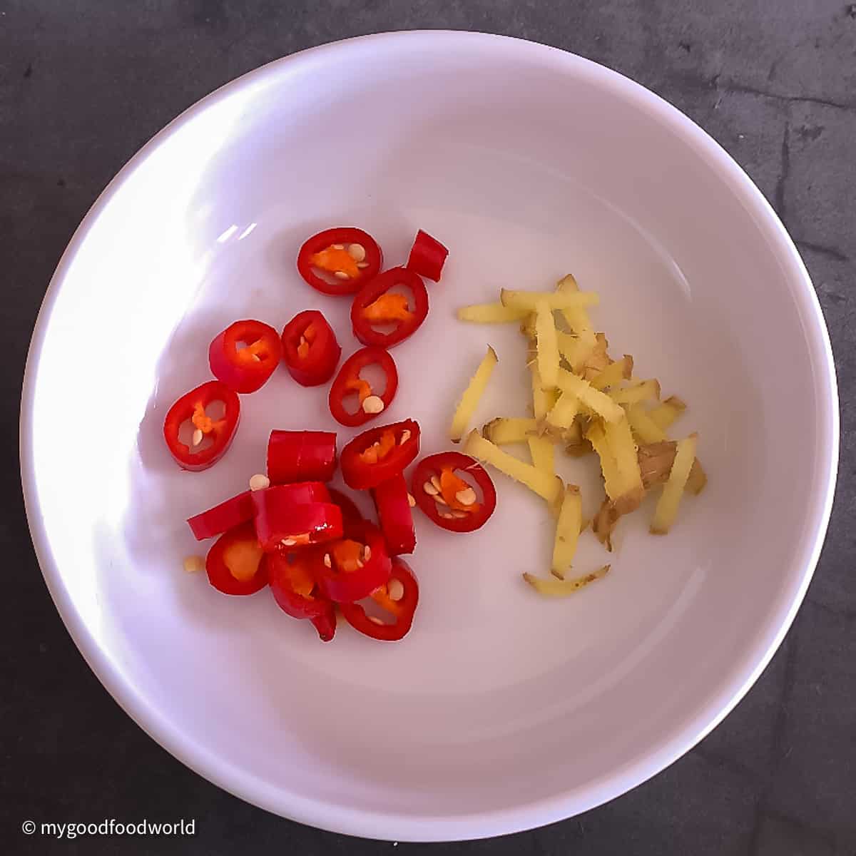 Chopped ginger and fresh red chili pepper are placed in a round white bowl.