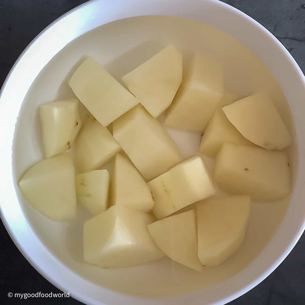 Diced potato soaking in water in a round white bowl.