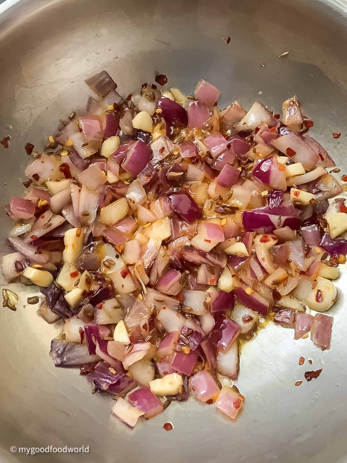 Diced onion and garlic are frying in oil along with some cumin seeds and red pepper flakes.