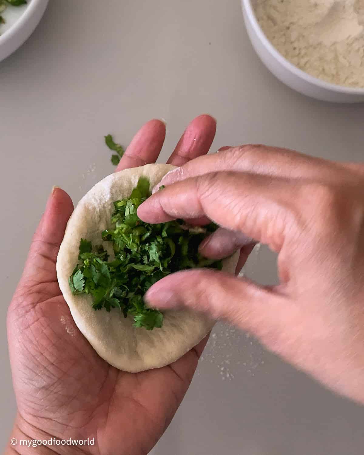 Finely chopped cilantro and green chili pepper mixture being placed in a disc of dough. The dough disc is being held in the palm of a person's hand.