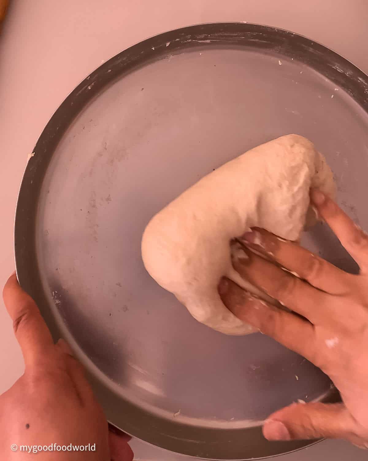 A soft, kneaded dough for making bullet naans is being folded with a persons fingers so that it can be kneaded again.