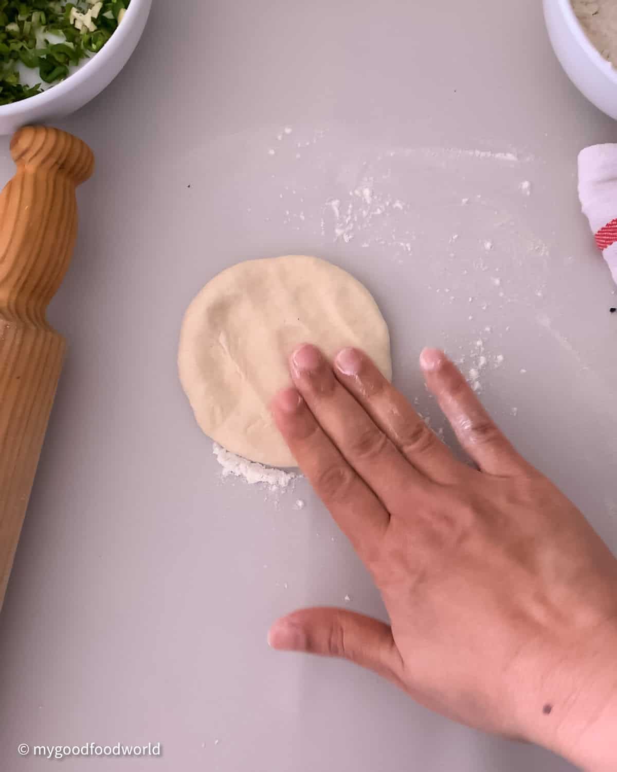 A hand is shown to be pressing a ball of dough to make a disc using three of the five fingers.
