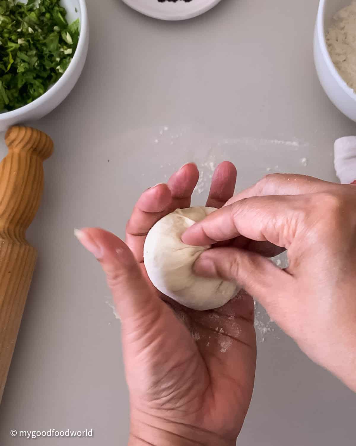 A dough ball that has been stuffed with a filling is being pinched to bring the ends together and make a leak-proof dumpling-like shape.