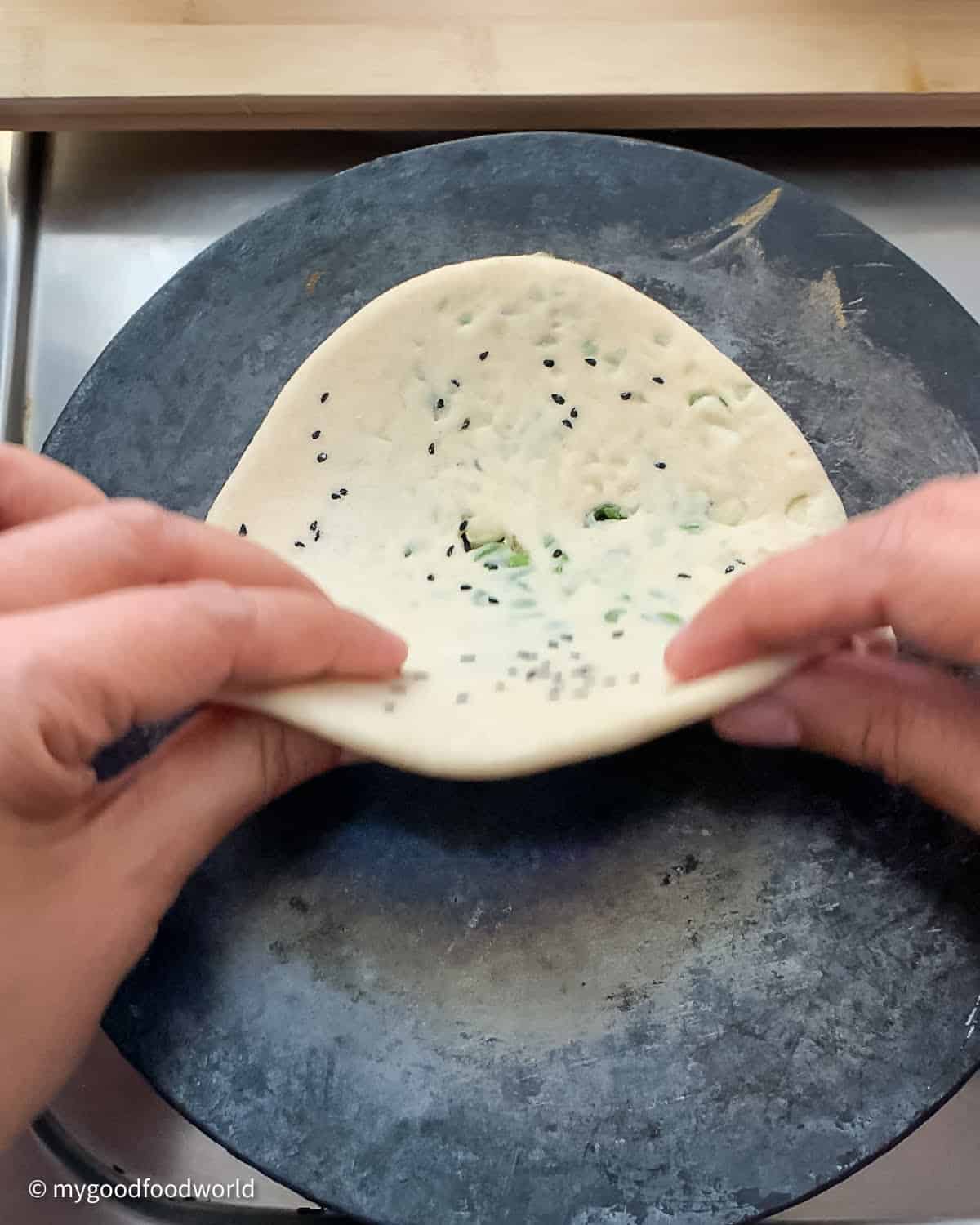 A rolled out bullet naan bread is being placed on a hot cast iron pan for roasting.