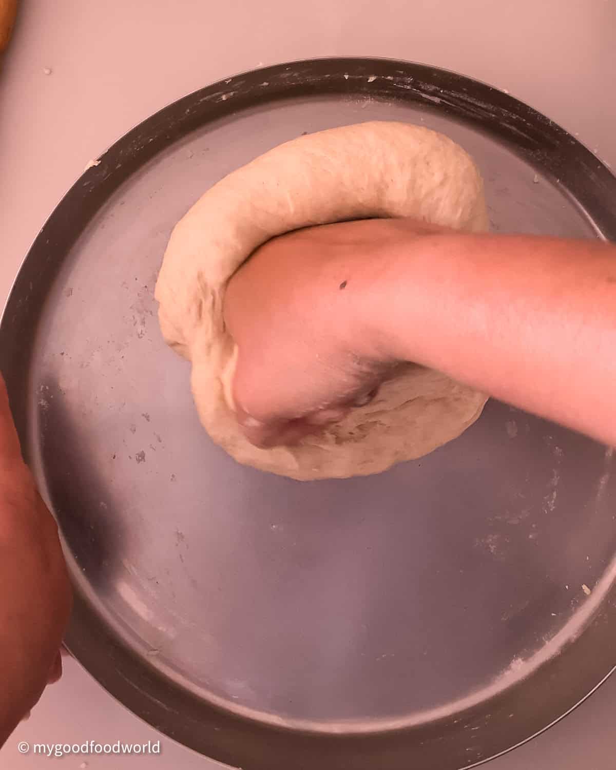 A brown coloured hand is shown to be pressing down a ball of dough which is placed on a stainless steel.