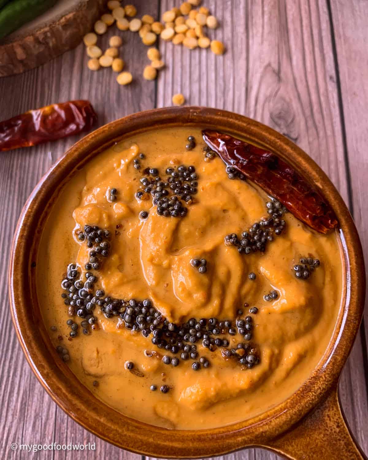Roasted Bengal gram chutney is placed in a brown colored ceramic bowl with handle. The chutney is garnished with some brown mustard seeds fried in oil and a fried red chili.