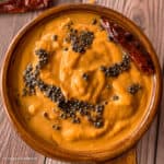 Split chickpea lentils, also known as chana dal, are ground to make a smooth chutney. The chutney is served in a round brown dish and with garnishing of tempered whole spices.