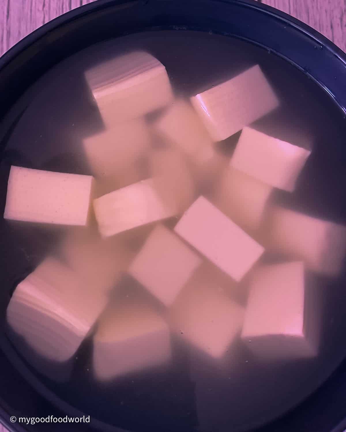 Cubes of paneer, Indian cottage cheese - cut into, roughly 1 inch each, are immersed in water in a round bowl.