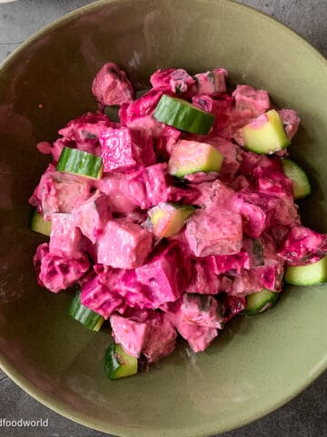Bite sized pieces of oven roasted beets and cucumbers are tossed together and served in a olive-green colored bowl. The salad has a bright pink dressing.