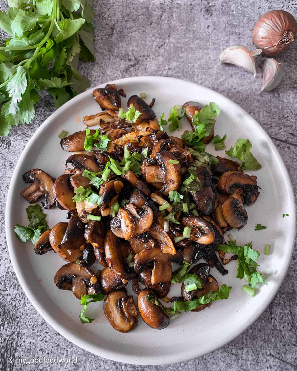 Caramelized onions and mushrooms in garlic butter, garnished with fresh cilantro, served on a round white plate.