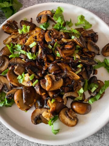 Onions and mushrooms caramelized in butter with garlic and spices. This dish is served in a round white plate. Some chopped cilantro is placed on the top as garnish.