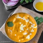 Shahi paneer recipe is made into a creamy and flavorful main dish. It is served in a bowl which is placed on burlap. Round sliced red onions are placed in a white bowl next to the curry bowl.