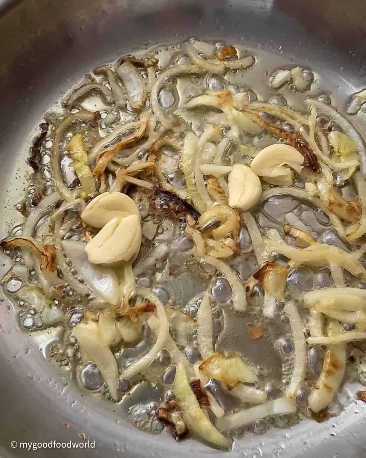 Slices of onions frying in butter until they are golden brown in color. Some smashed garlic pods are added to the caramelizing onions.