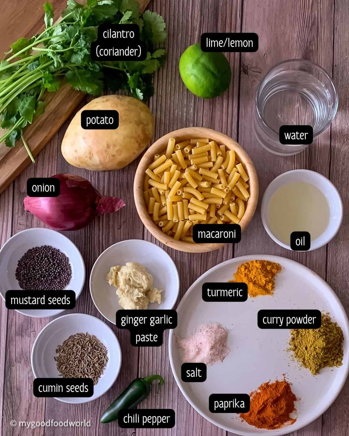 Ingredients for pasta and potato recipe such as macaroni, onion, ginger garlic pasta, cumin, lemon, chili pepper, potatoes, and oil are placed in small white bowls and plates and arranged next to each other on a brown background.