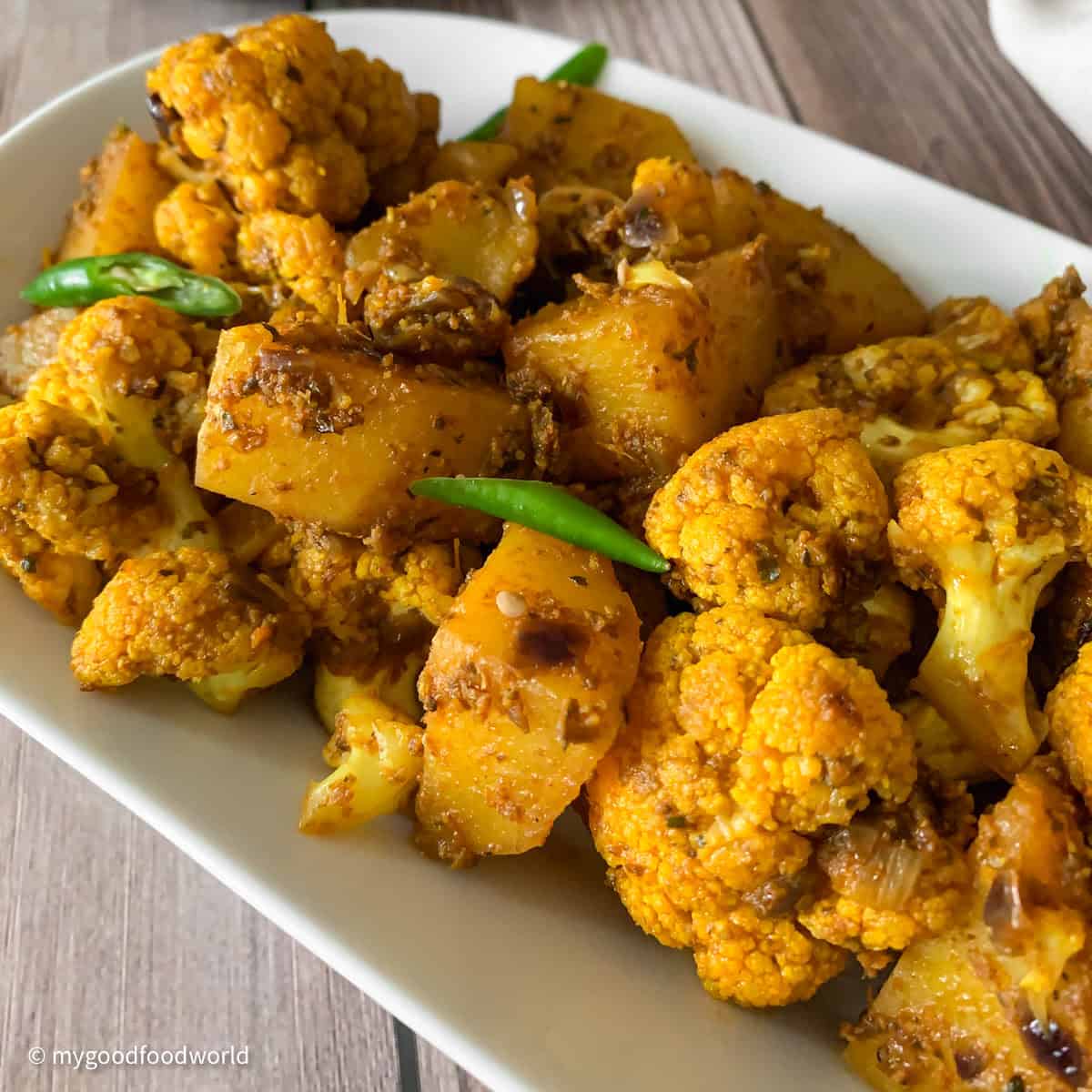 A plate of Indian cauliflower and potato curry on a wooden table.