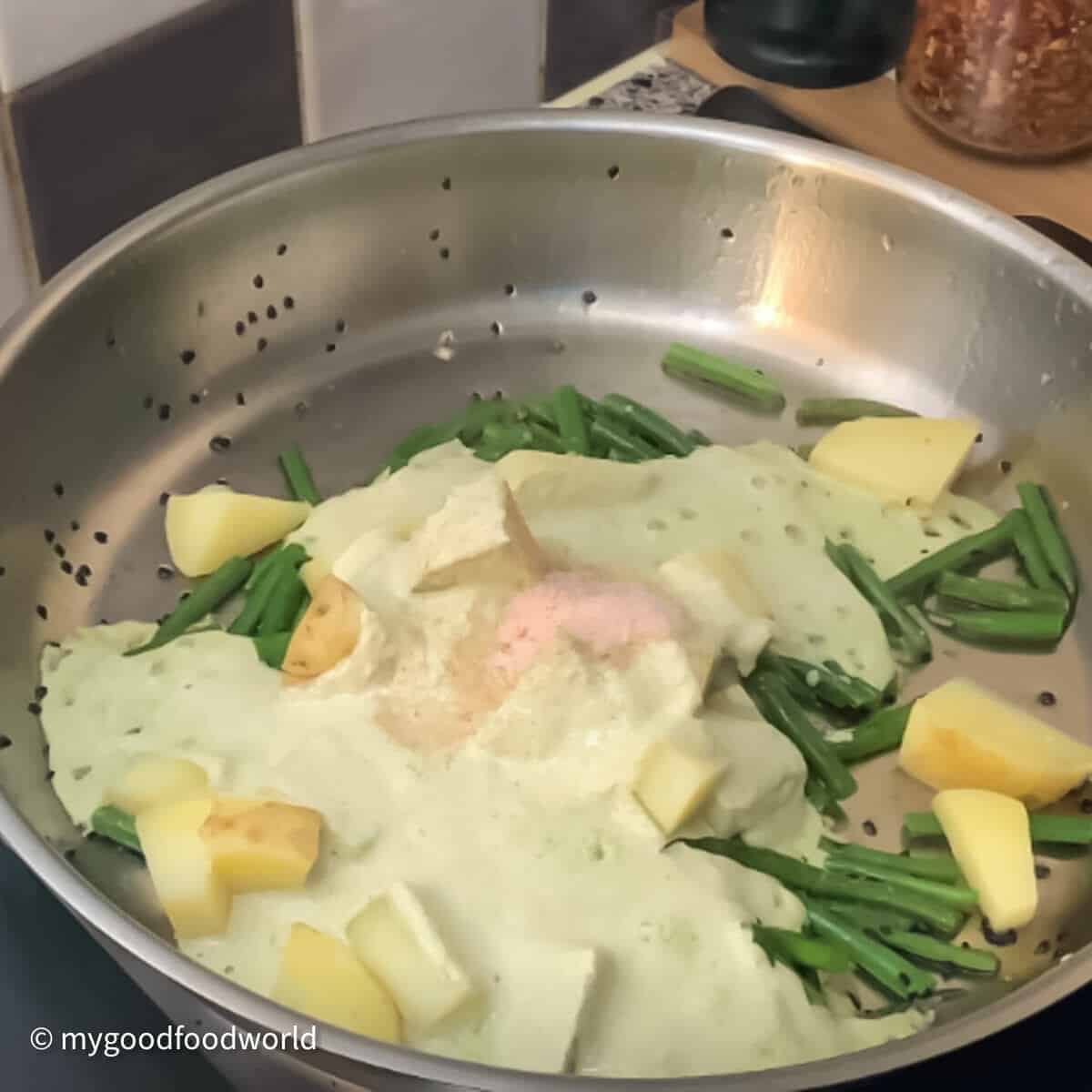 A photo of a skillet with a creamy sauce, green beans, and potatoes cooking on a stovetop.