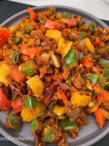 Diced colored capsicum sautéed with spices and onions are placed on a grey round plate.
