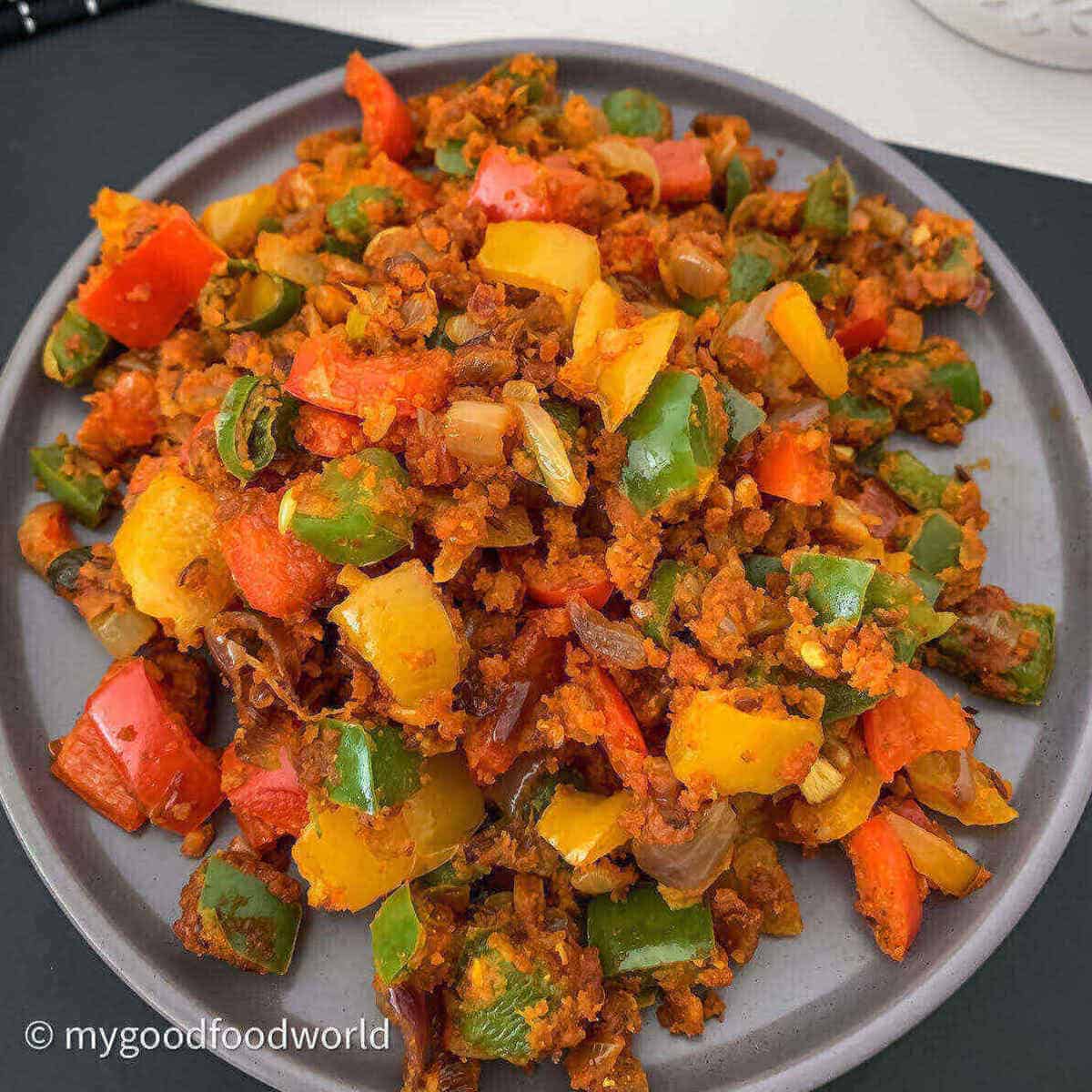Diced colored capsicum sautéed with spices and onions are placed on a grey round plate.