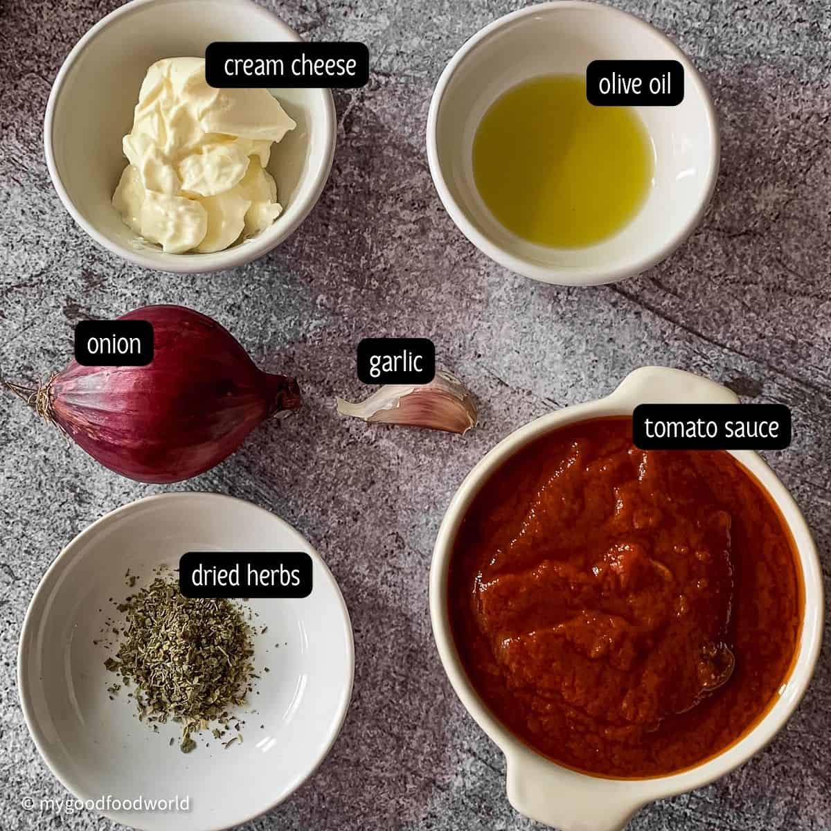 Ingredients for a sauce recipe such as cream cheese, olive oil, dried herbs, tomato sauce, and garlic are placed in bowls and on a grey background.