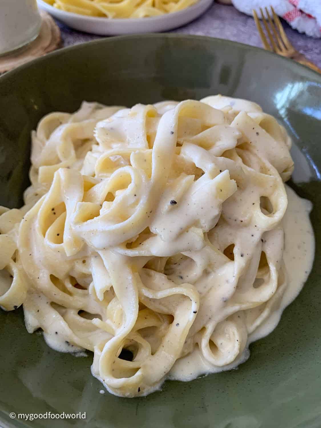 Some fettucine pasta thickly coated in a white colored creamy sauce with seasoning is plated in a green round bowl.