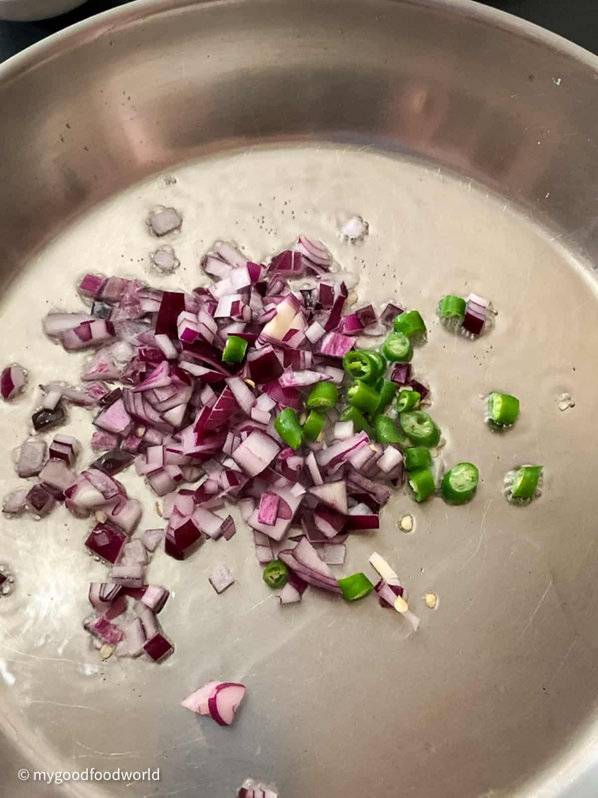 Red onions and green chili peppers frying in a pan on a stovetop.