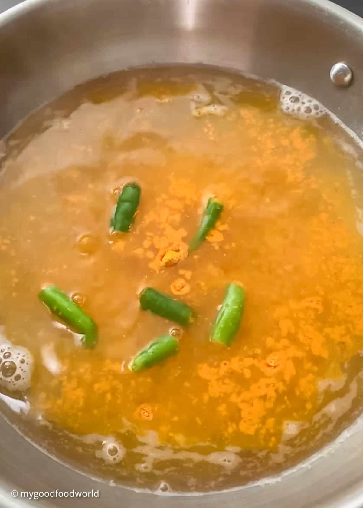 Some water with turmeric and chopped green chili peppers is cooking in a steel wok.