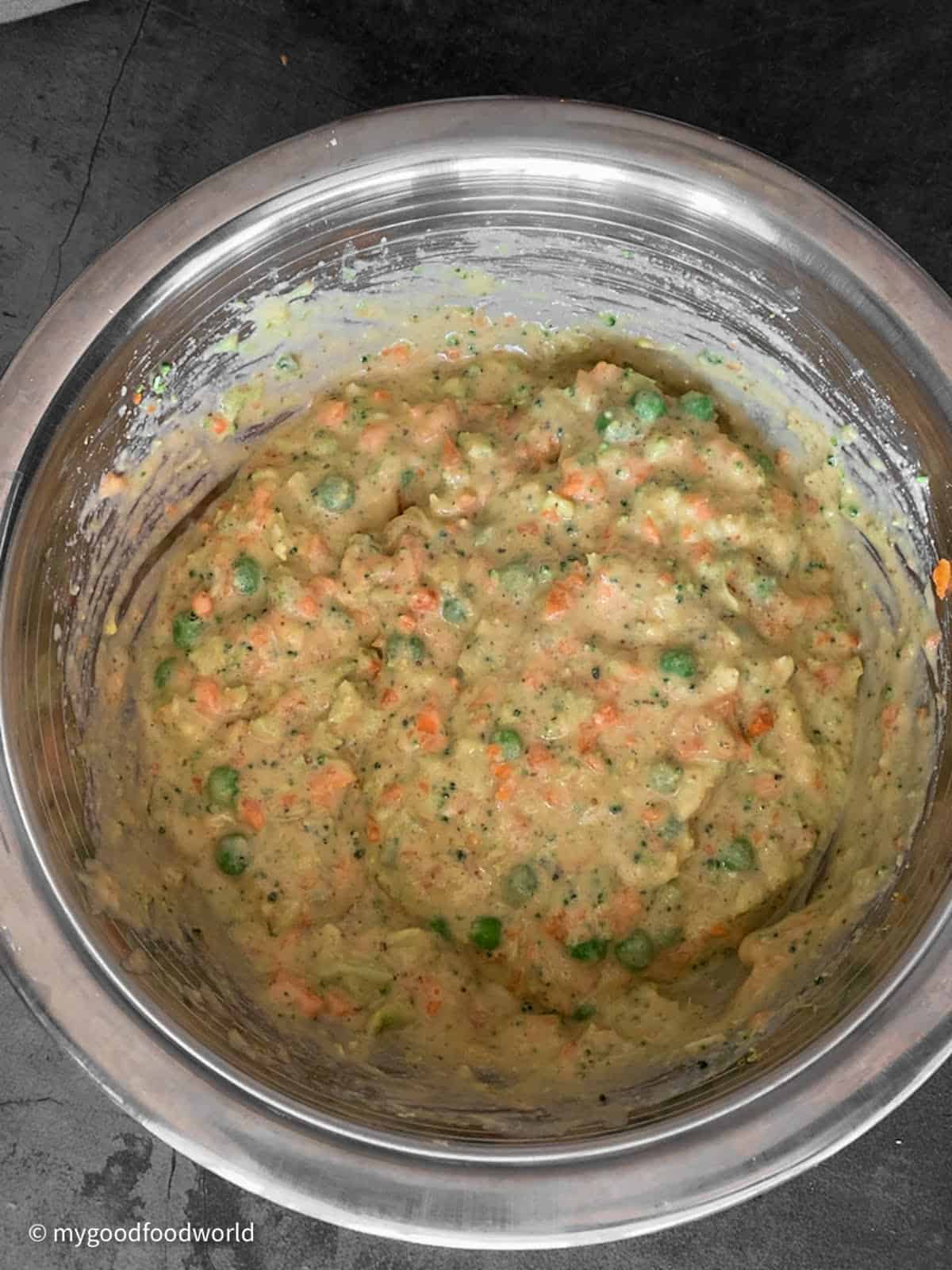 Muffin batter with chopped vegetables and spices has been mixed and kept ready in a steel bowl.