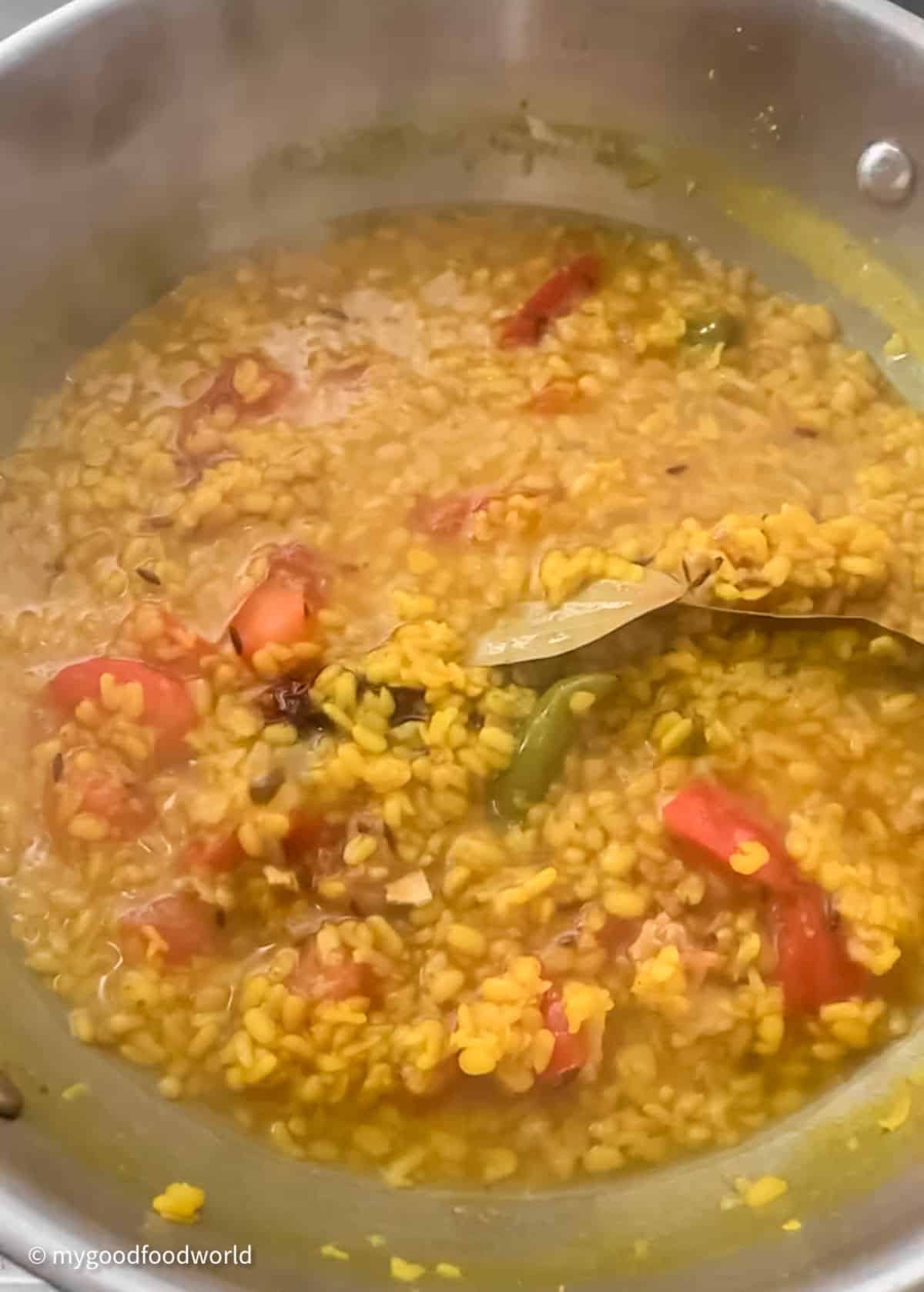Bhaja moong lentils with tomatoes, bay leaves and other spices is cooking in a pan.