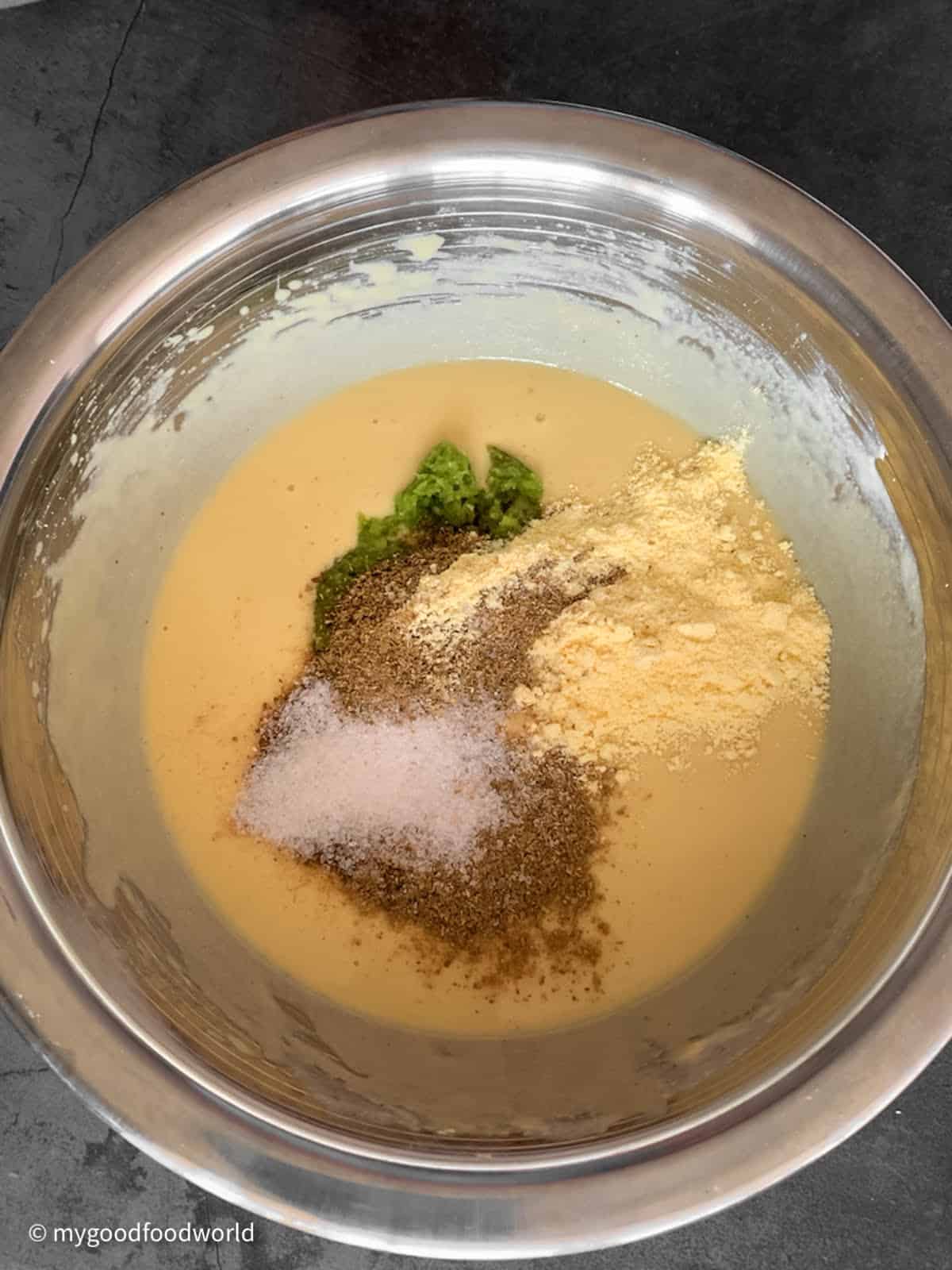 Powdered spices and salt placed in a heap on a yellow colored batter that has been smoothly whisked.