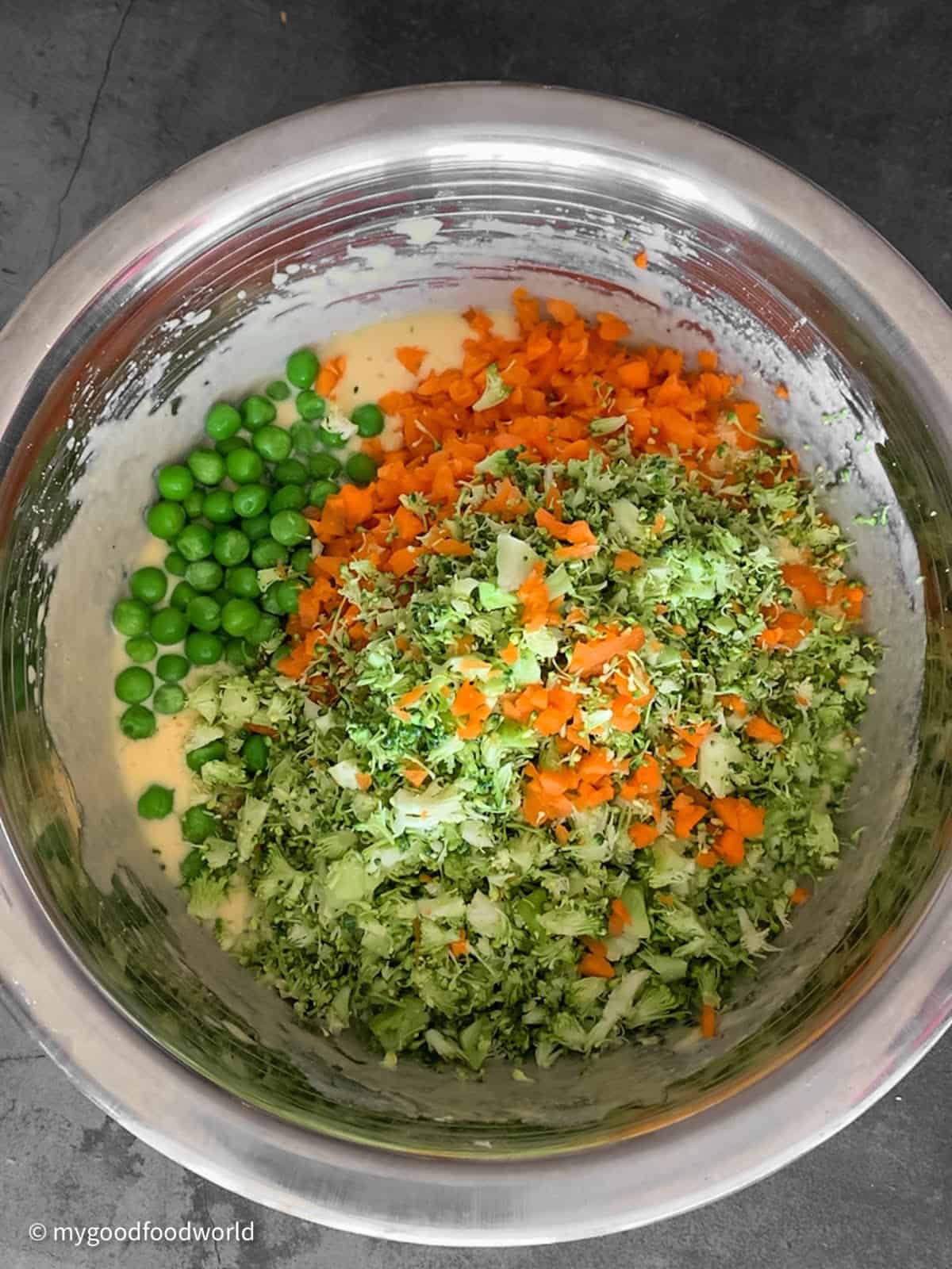 Finely chopped vegetables and peas are added to batter in a deep stainless steel bowl.