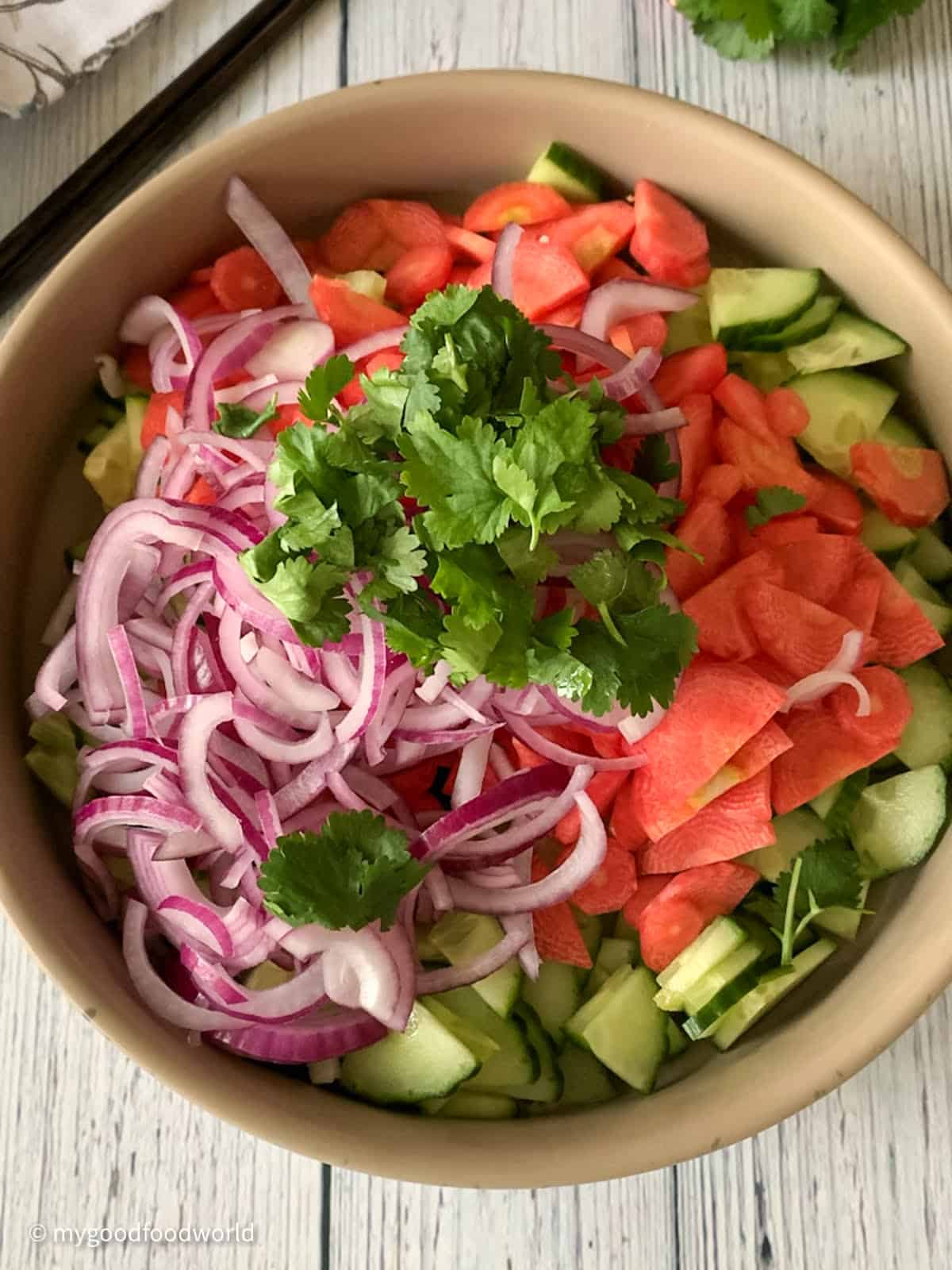 Thinly sliced cucumbers, carrots, and red onion are placed in a wide bowl. Some chopped fresh cilantro is placed on top of the sliced veggies.