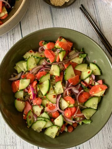 Salad of carrots and cucumber and red onions is served in a bowl. The salad has some toasted sesame seeds and red pepper flakes garnish.