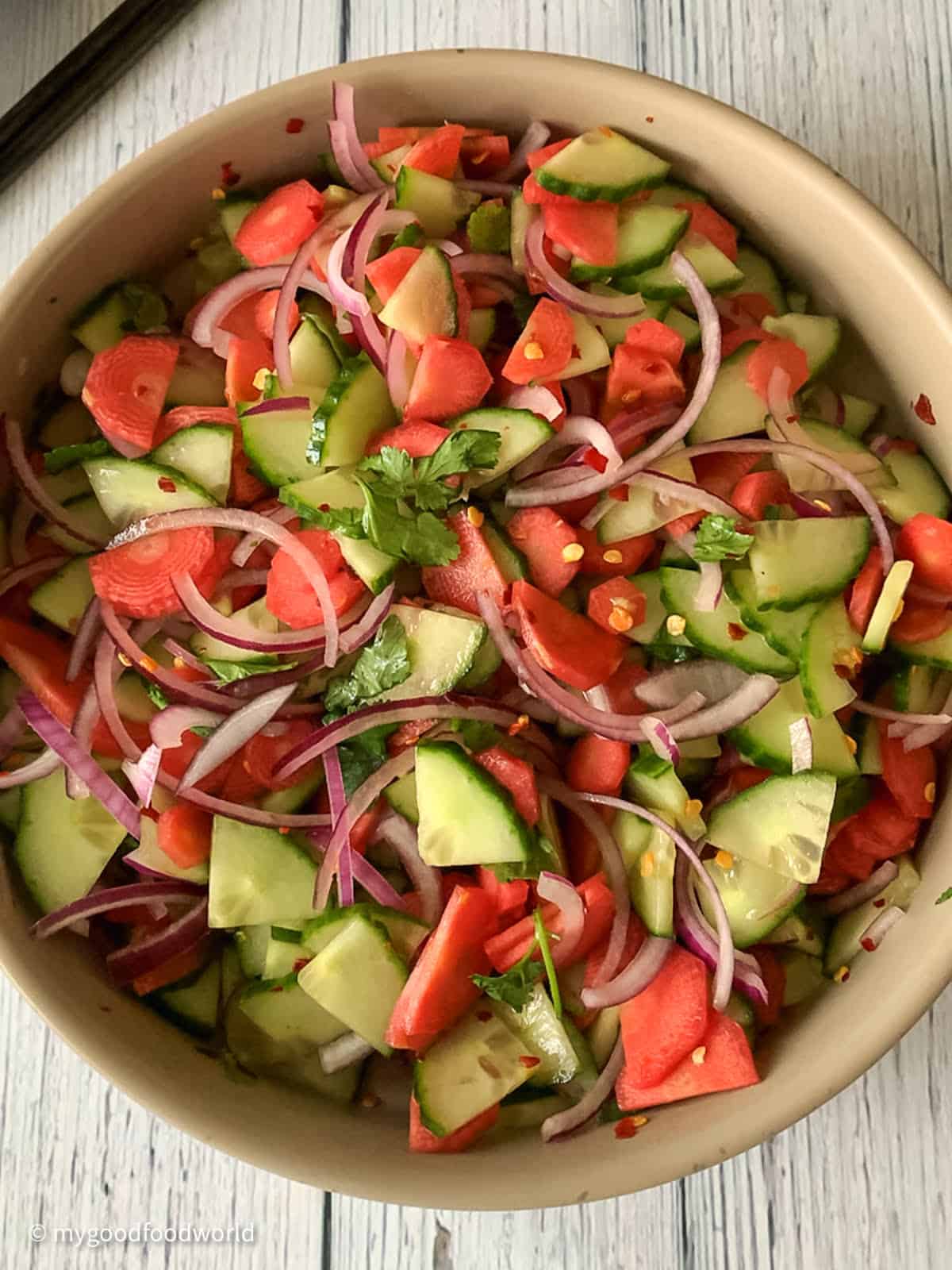 Simple carrot and cucumber salad with slivers of red onion and some red pepper flakes is served in a wide serving bowl.