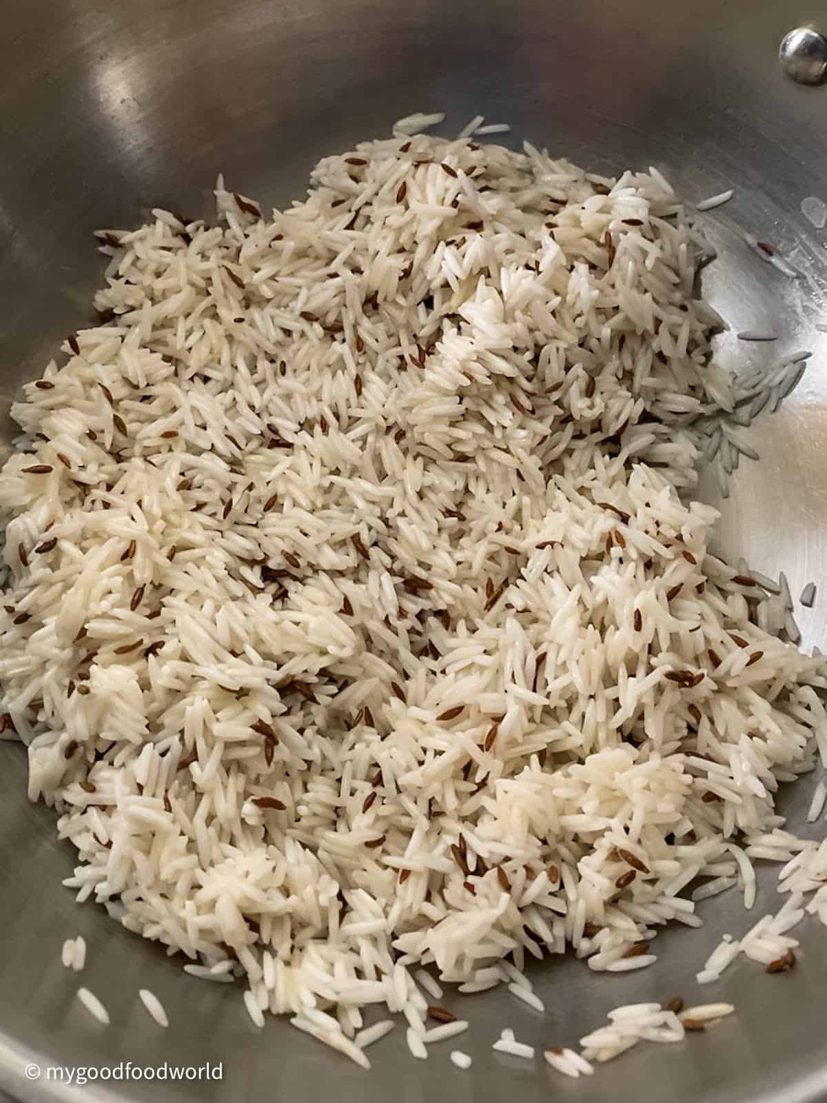 Basmati rice and whole cumin seeds are tossed together in a steel pan.