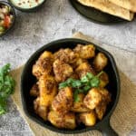 Aloo jeera dry sabzi is served in a black cast iron pan. The dish is garnished with a spring of fresh cilantro.
