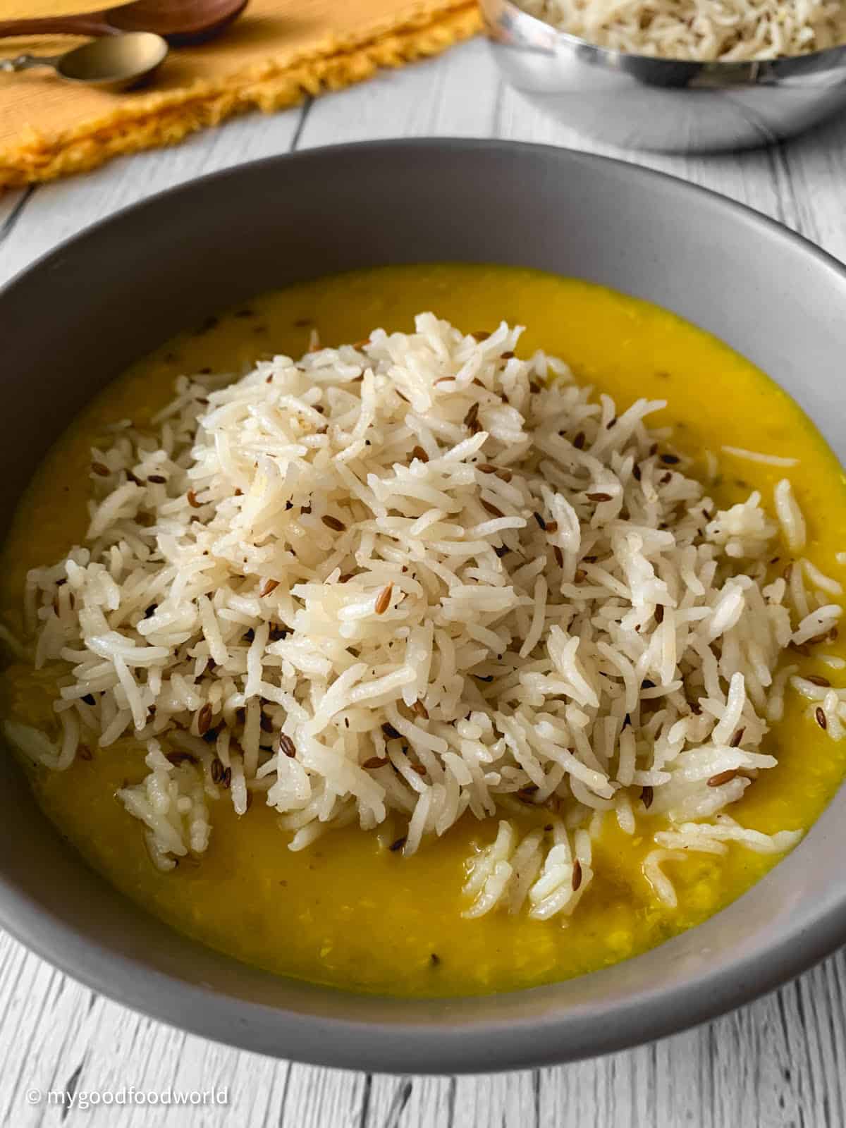 In a round grey colored bowl, some jeera rice is served yellow dal.