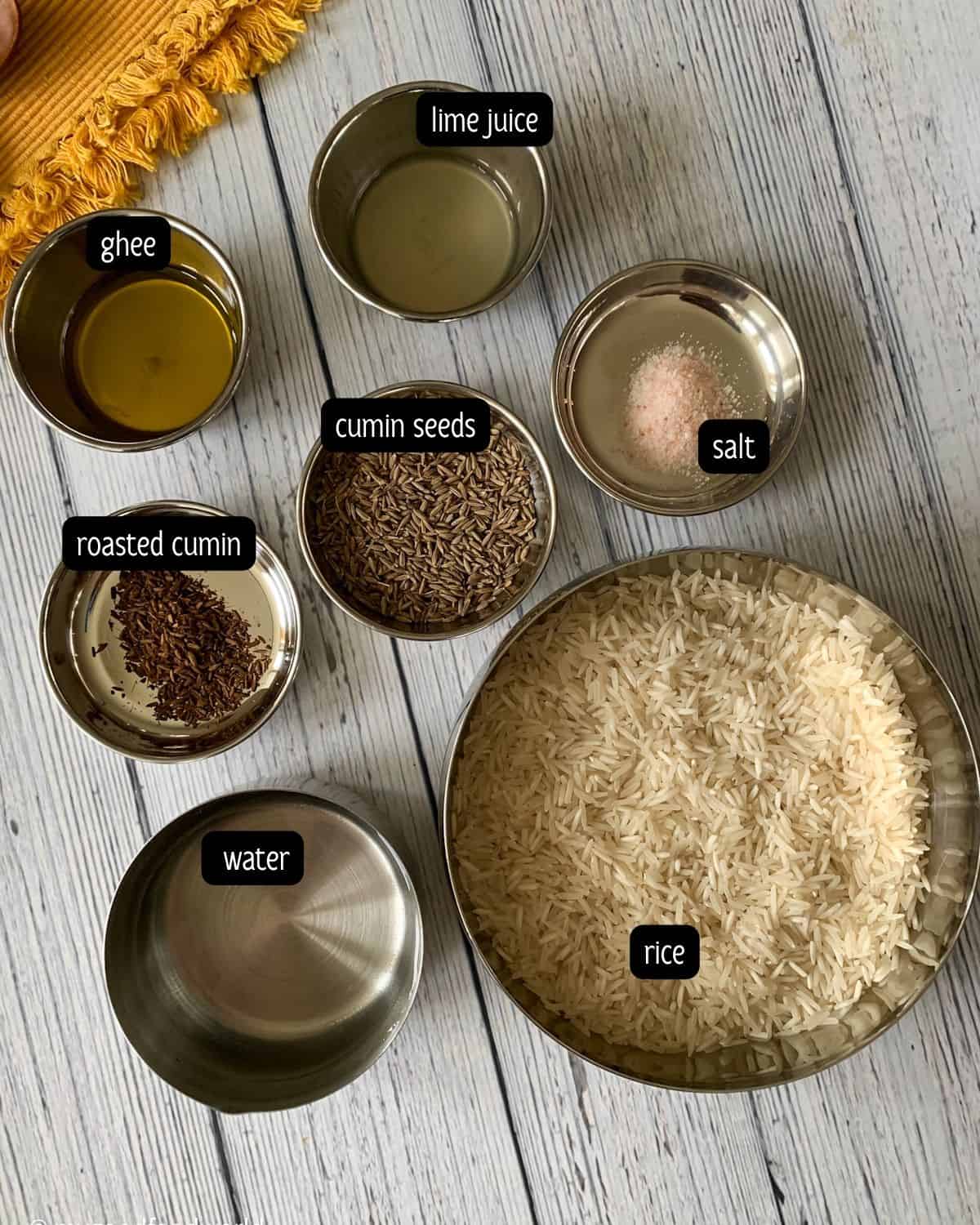 Ingredients such as rice, water, cumin seeds, salt, ghee, lime juice, and roasted cumin are placed in steel bowls and plates.
