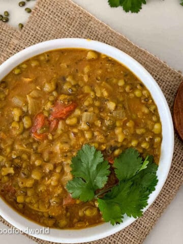 A bowlful of mung bean curry is served in a bowl with some cilantro leaves garnished on the top.