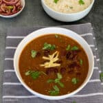 Homemade Punjabi-style rajma recipe is made and served in a round white colored bowl. Some slivers of ginger and chopped cilantro are garnished on top.