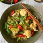 Asian-style noodle soup with vegetables and garnishes is served in a round green bowl.