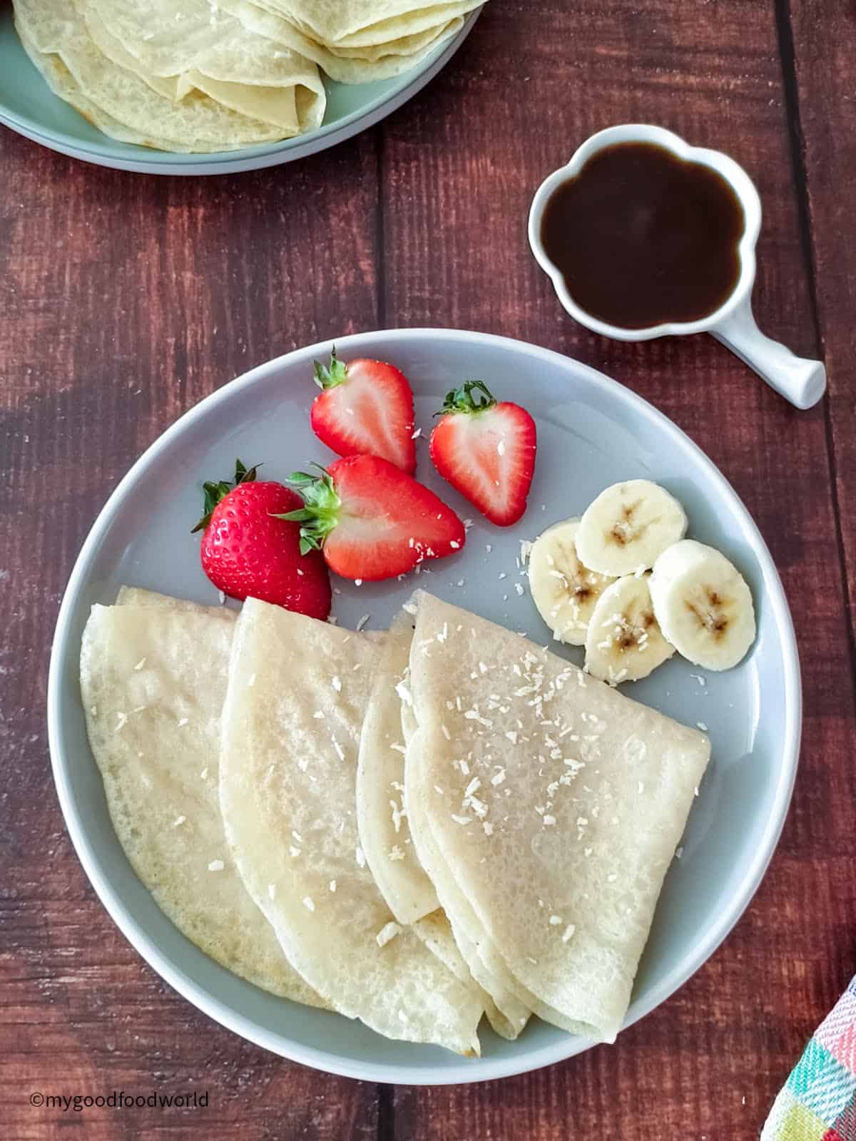 Soft, homemade crepes are folded and placed on a plate along with some bananas and strawberries.