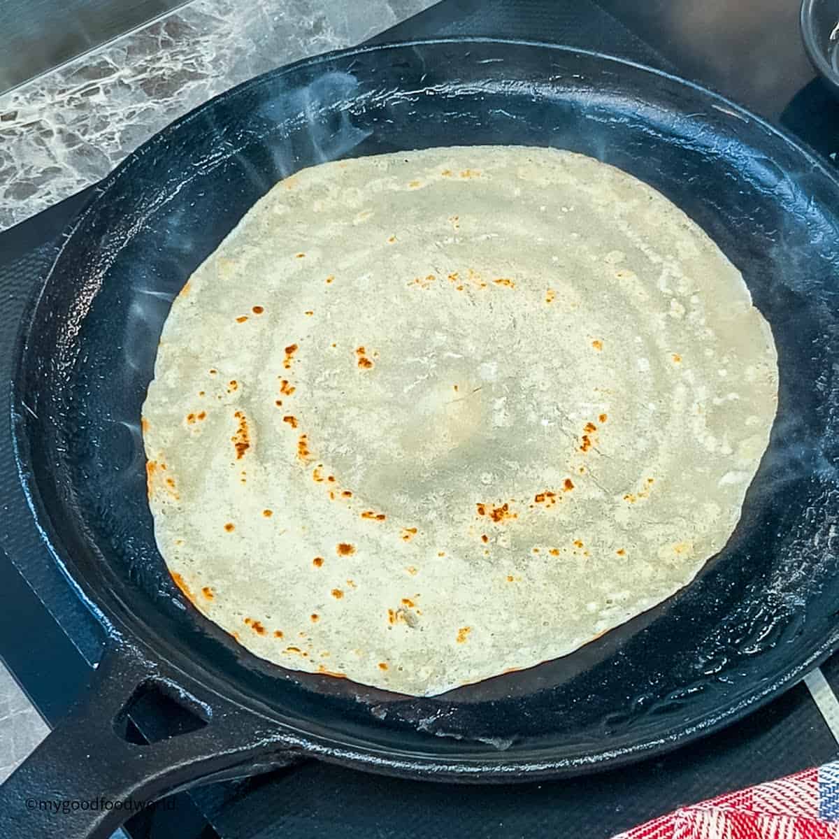 A plain flour crepe is being cooked in a skillet on a stove.