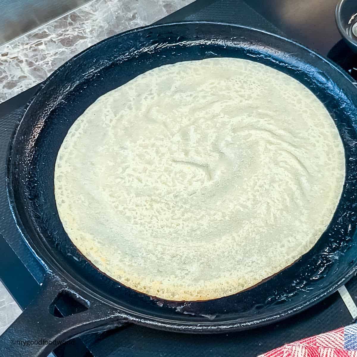 A dairy-free crepe is being cooked in a skillet on a stove.