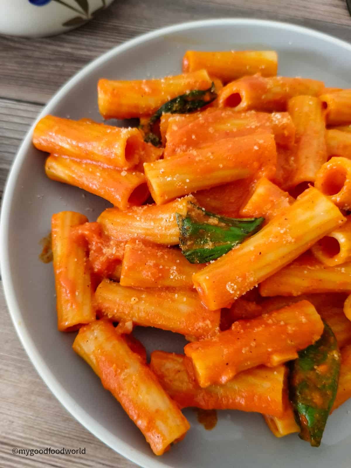 Rigatoni pasta with red pepper sauce and fresh basil is served on a plate.