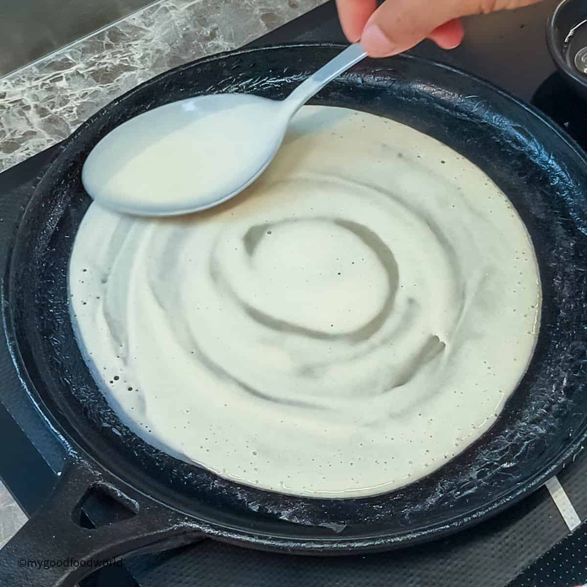 A person is stirring a coconut crepe in a skillet.