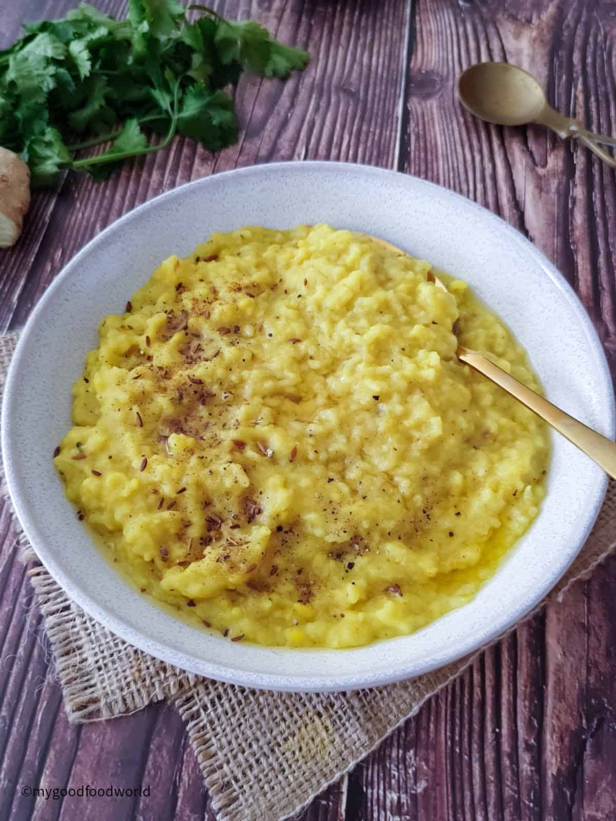 Simple mung lentils and rice kitchari sits in a bowl with ghee and cumin garnish.
